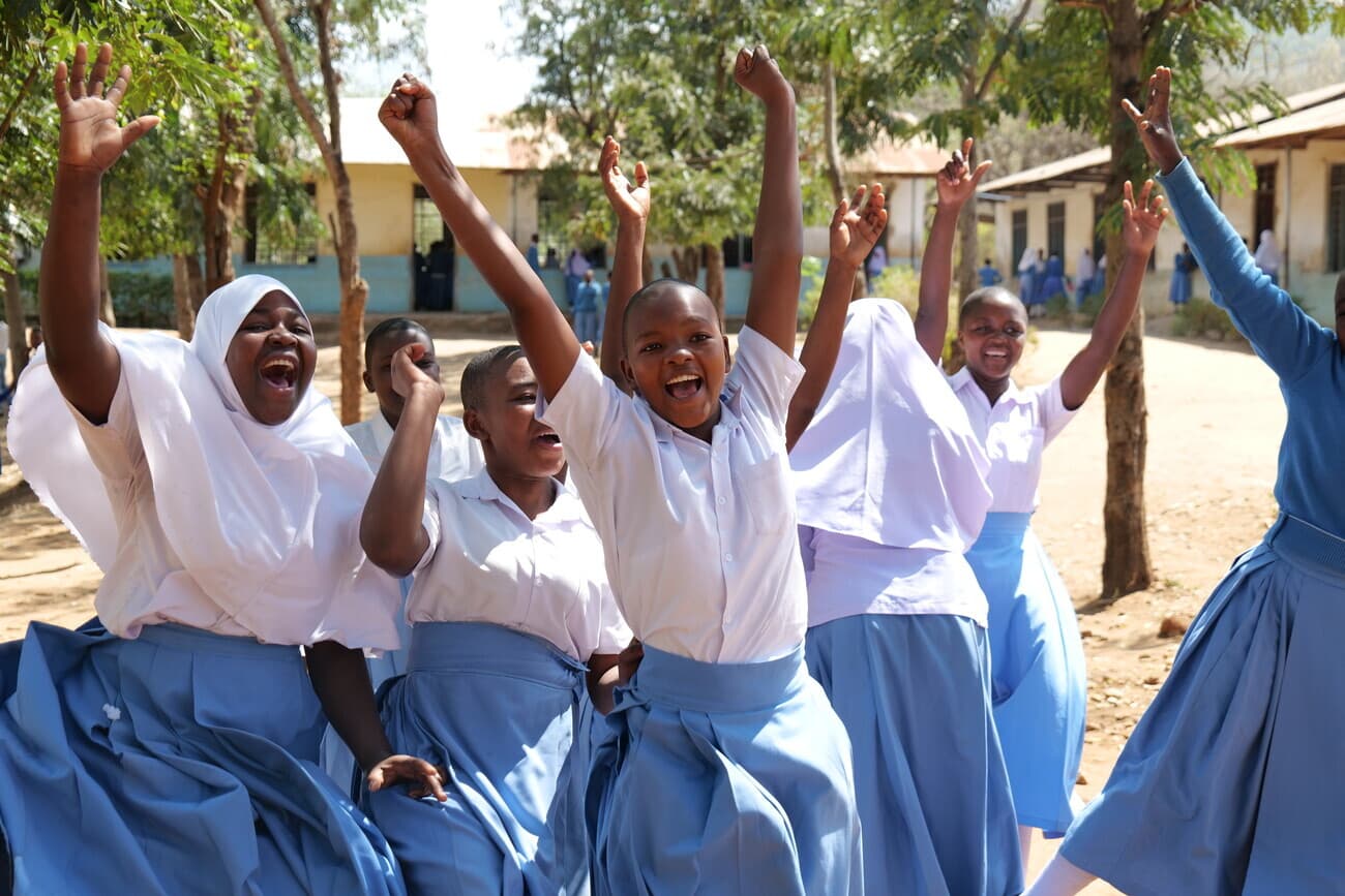 Young girls in school uniforms celebrating with arms raised at a school in Africa